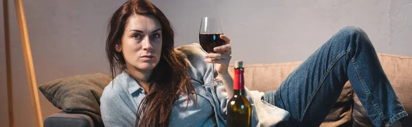 沮丧的女人一边躺着 一边看着相机 手里拿着一杯红酒 一面横幅 — 图库照片