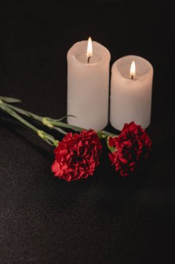 Kırmızı karanfil çiçekleri ve siyah arka planda mumlar, cenaze konsepti.