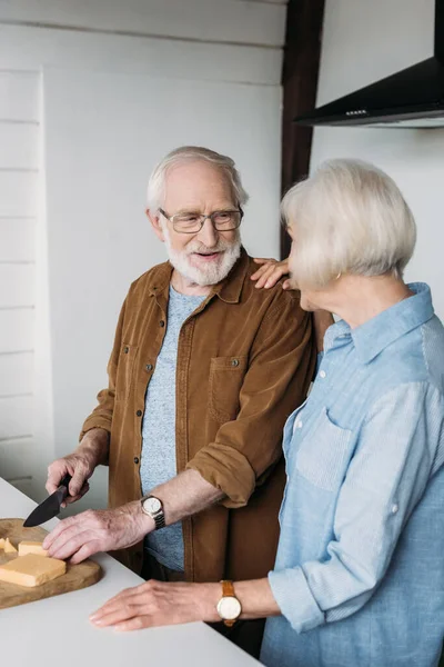 Sonriente Hombre Mayor Mirando Mujer Mientras Corta Queso Tabla Cortar — Foto de Stock