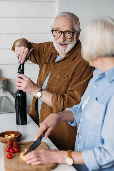Счастливый Пожилой Муж Смотрит Жену Открывая Бутылку Вина Штопором Кухне — стоковое фото