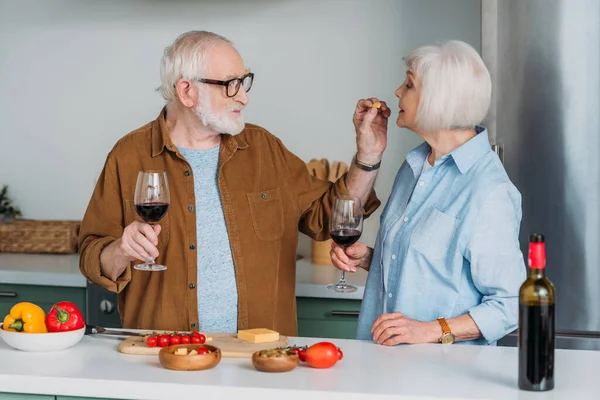 Smiling Senior Man Wine Glass Feeding Wife Piece Cheese Kitchen — Stock Photo, Image