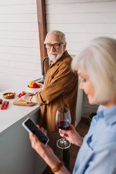 Sonriente Anciano Marido Mirando Esposa Mientras Cocina Cena Cocina Borrosa —  Fotos de Stock