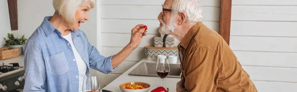 Side View Happy Elderly Wife Feeding Husband Cherry Tomato Kitchen — Stock Photo, Image