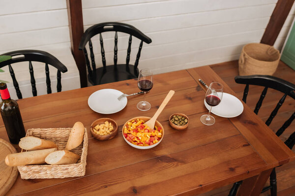 high angle view of served table with vegetarian dinner, baguette in basket and wine in kitchen