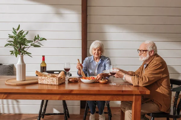 Esposa Sênior Feliz Com Espátula Servindo Salada Para Marido Mesa — Fotografia de Stock