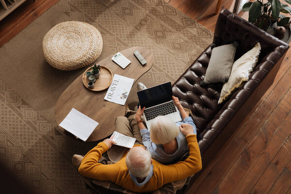 верхний вид пожилой пары с помощью ноутбука во время объятий на диване в гостиной