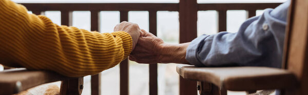 cropped view of senior couple holding hands on terrace on blurred background, banner