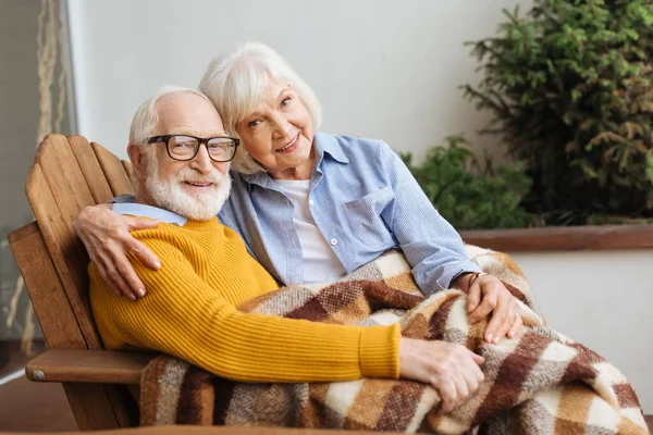 Happy Senior Couple Plaid Blanket Looking Camera While Hugging Armchair — Stock Photo, Image