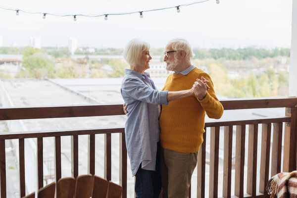 happy senior couple looking at each other while dancing on terrace on blurred background