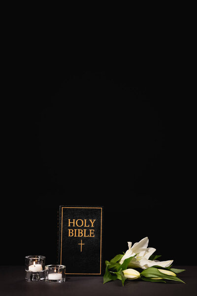 lily, candles and holy bible on black background, funeral concept