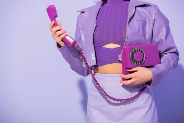 Mor renkli arka planda, bebek stili giyinmiş, retro telefonlu genç bir kadın görüntüsü.