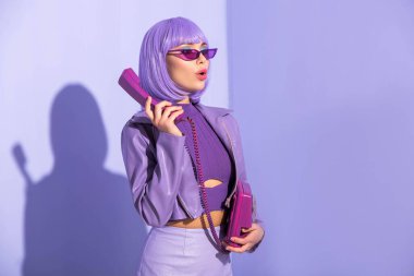 Mor renkli arka planda retro telefonlu oyuncak bebek gibi giyinmiş genç bir kadın.