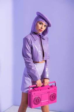 Mor renkli arka planda pembe retro kayıt cihazıyla poz veren bebek gibi giyinmiş genç bir kadın.