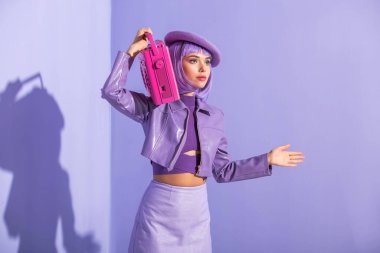 Mor renkli arka planda pembe retro kayıt cihazıyla poz veren bebek gibi giyinmiş genç bir kadın.
