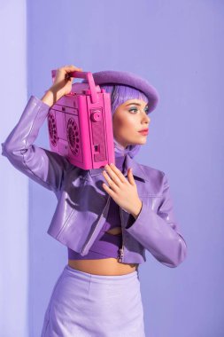 Mor renkli arka planda pembe retro kayıt cihazıyla poz veren bebek gibi giyinmiş genç bir kadın.