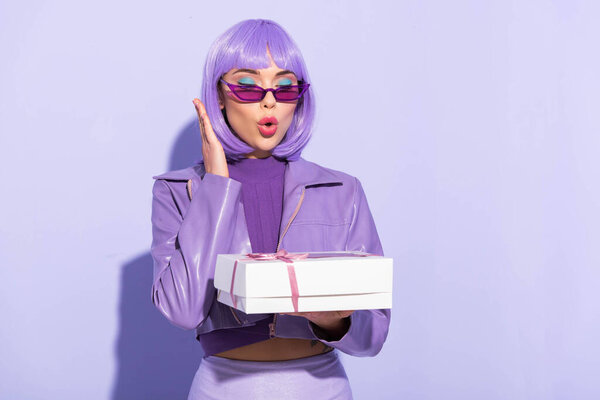 shocked young woman dressed in doll style with cupcake box on violet colorful background