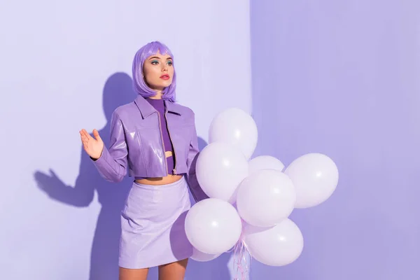 紫色のカラフルな背景の風船で人形のような服を着た若い女性 — ストック写真