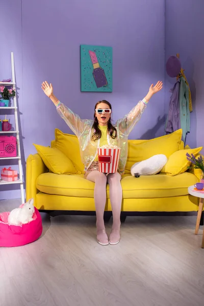 young woman posing as doll with popcorn in 3d glasses on yellow couch