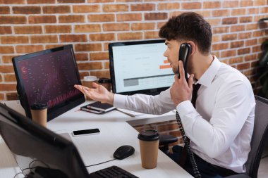 İş adamı telefonda konuşuyor ve finansal kursların çizelgeleriyle bilgisayara işaret ediyor 