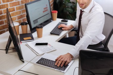Akıllı telefon ve ofis haberleri yakınlarındaki finansal stokları kontrol ederken bilgisayar ve dizüstü bilgisayar kullanan işadamlarının görüntüsü kırpıldı 