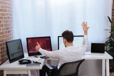 İş adamının ekranlarda finans piyasası grafikleriyle bilgisayarların yanında baş parmağını göstermesinin arka planı 