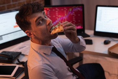 İş adamı akşam ofiste pizza yerken kameraya bakıyor. 
