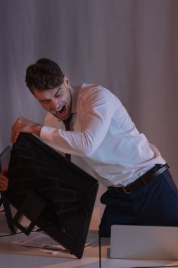 Sinirli iş adamı akşam vakti ofise bilgisayar atıyor.