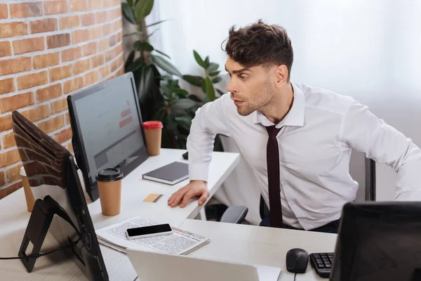 Young Businessman Looking Computer While Checking Finance Stocks Smartphone Newspaper — Stock Photo, Image