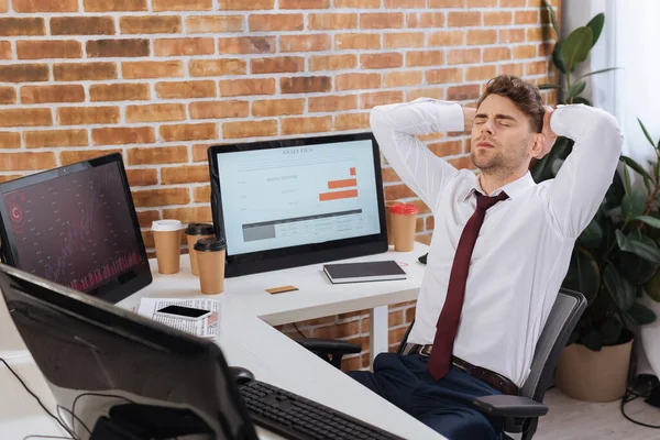 Wyczerpany Biznesmen Siedzący Pobliżu Komputerów Wykresami Kursów Finansowych Monitorze — Zdjęcie stockowe