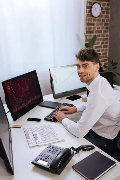 Pebisnis Tersenyum Menggunakan Komputer Dengan Grafik Pada Monitor Dekat Telepon — Stok Foto
