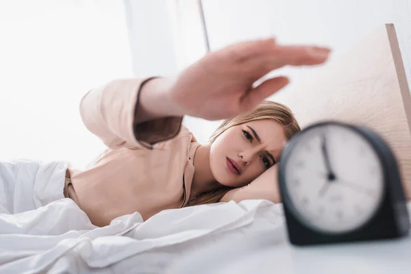 Displeased Young Woman Reaching Alarm Clock Bedside Table Blurred Foreground — Stock Photo, Image