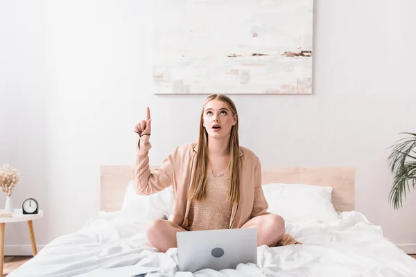 surprised young freelancer in silk robe having idea near laptop on bed