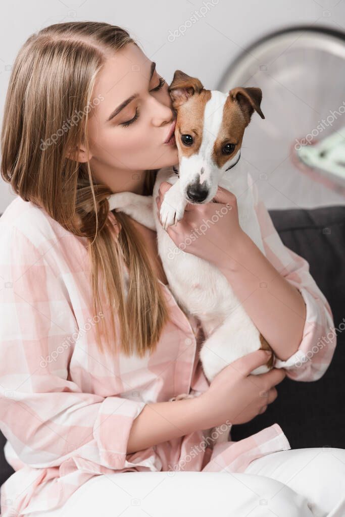 young woman holding in arms and kissing jack russell 