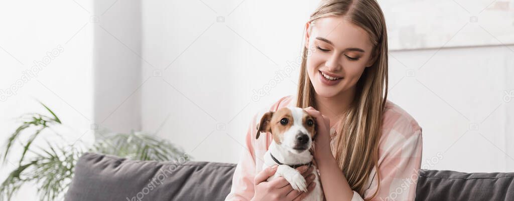 smiling woman cuddling jack russell terrier at home, banner