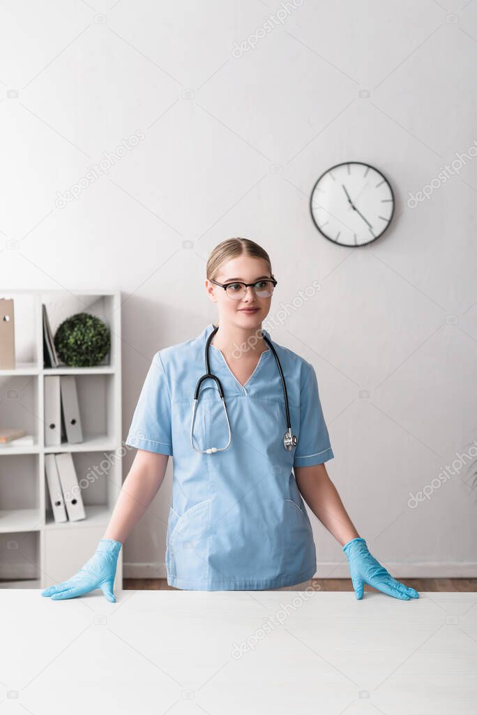happy young veterinarian in glasses and latex gloves standing near workplace 