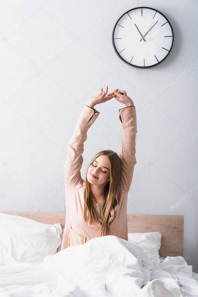 awake and positive woman in satin pajamas stretching in bed