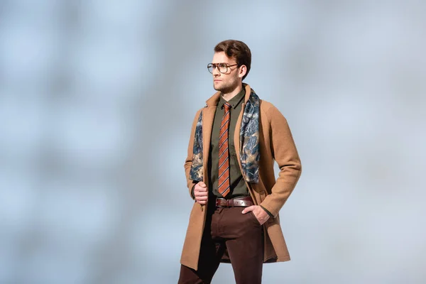 trendy man in winter outfit standing with hand in pocket on grey