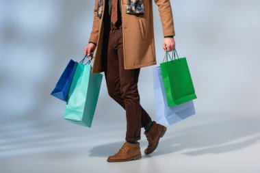 cropped view of customer in coat holding paper bags on grey clipart