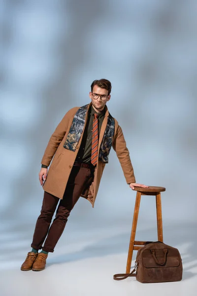 Gri Çantanın Yanındaki Ahşap Sandalyeye Yaslanmış Kışlık Kıyafetli Gözlüklü Modaya — Stok fotoğraf