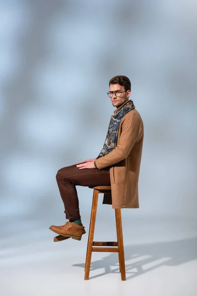 Stilvoller Mann Winteroutfit Und Brille Sitzt Auf Holzstuhl Auf Grau — Stockfoto