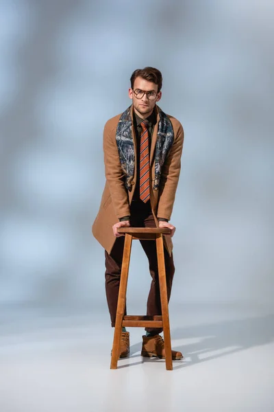 Stylish Man Winter Outfit Glasses Leaning Wooden Stool Grey Background — Stock Photo, Image