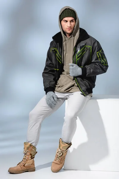 Full Length Trendy Man Hat Gloves Parka Sitting White Cube — Stock Photo, Image