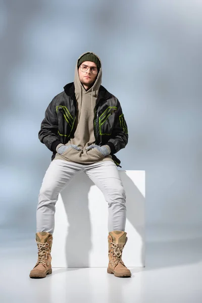 Full Length Young Trendy Man Hat Anorak Sitting Hands Pockets — Stock Photo, Image