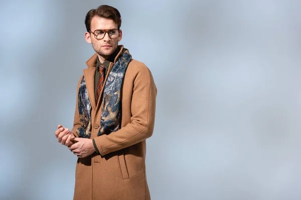 fashionable man in glasses, scarf and winter coat looking away on grey