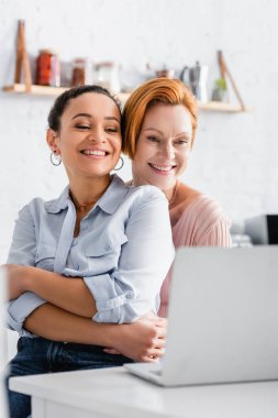 Mutfakta dizüstü bilgisayara bakan mutlu ırklar arası bir çift.