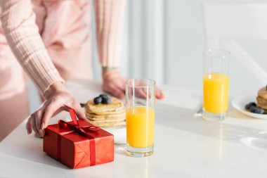 Sevgililer gününde kahvaltı servisi yapılan hediye kutusunu masaya koyan, arka planı bulanık bir kadın görüntüsü.