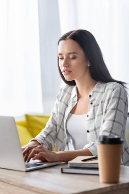 Dizüstü bilgisayarın yanında çalışan genç bir serbest yazar ve bulanık önplana çıkmak için kahve ve defterler.