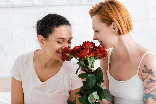 Feliz Afro Americana Mulher Cheirando Rosas Vermelhas Perto Ruiva Lésbica — Fotografia de Stock