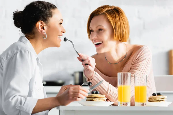 Cheerful Lesbian Woman Feeding African American Girlfriend Blueberry Breakfast — Stock Photo, Image