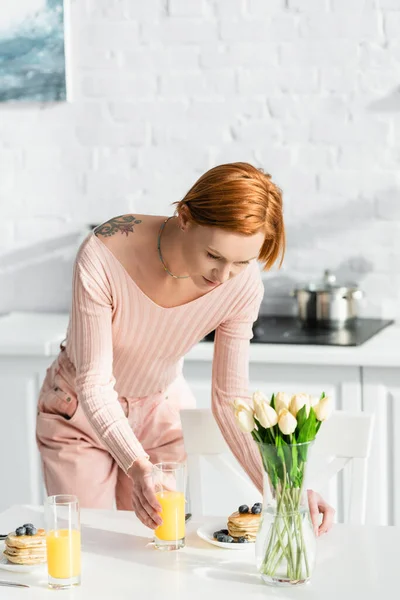 Ryšavý Tetovaný Žena Servírující Snídani Stole Blízkosti Tulipánů Kuchyni — Stock fotografie